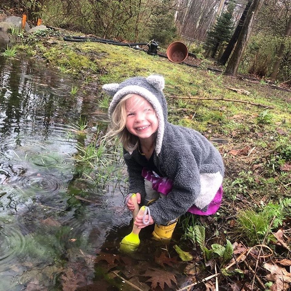 Child in a hooded jacket playing in a puddle with a toy