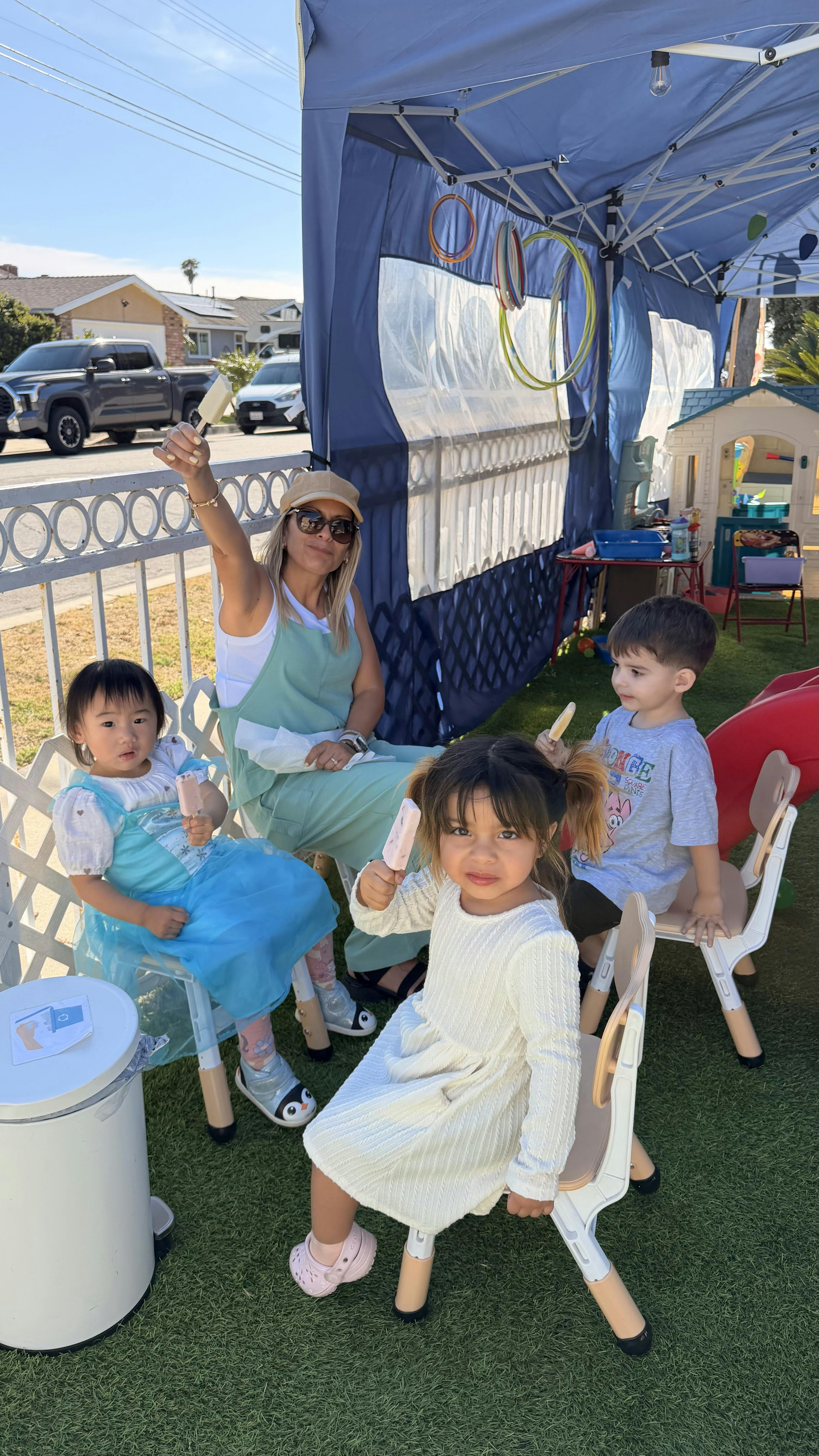 Adult and three children holding popsicles under a blue canopy