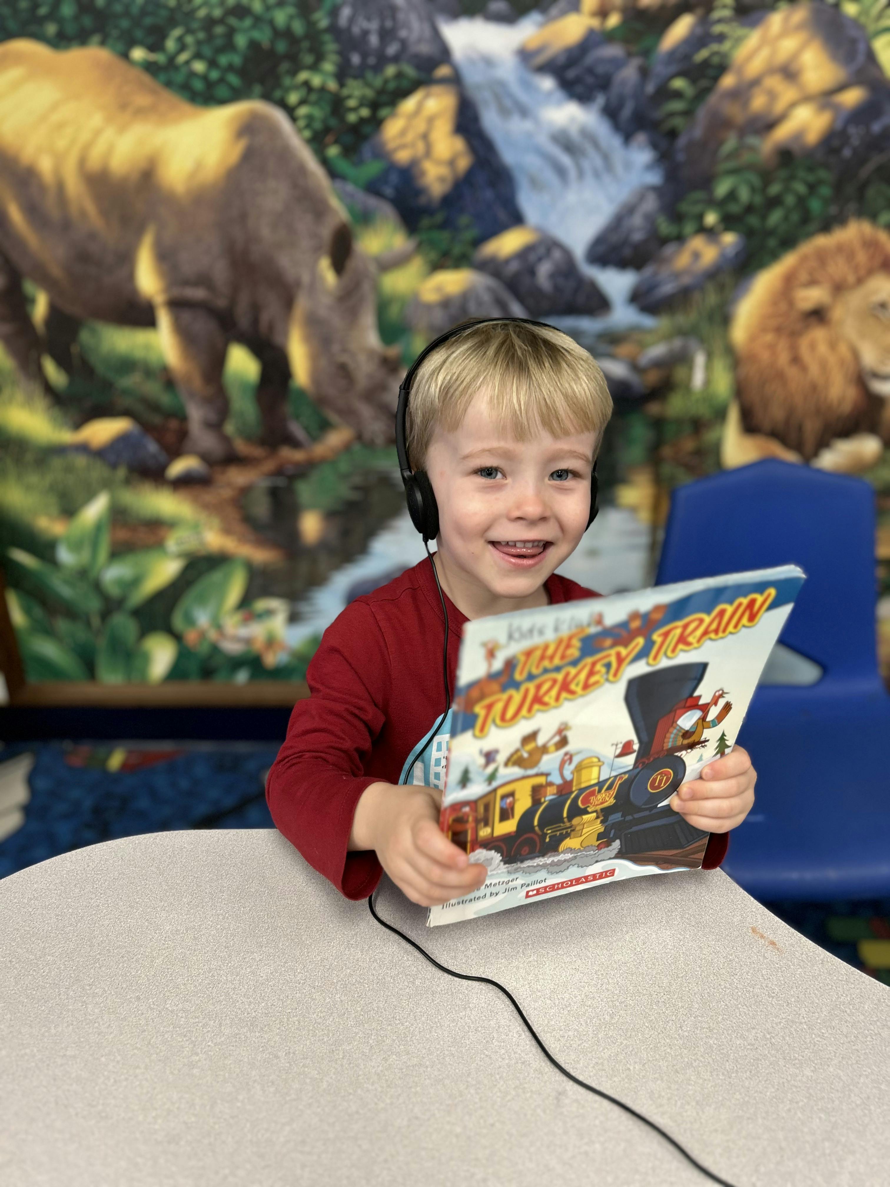 Child wearing headphones holding a book titled The Turkey Train