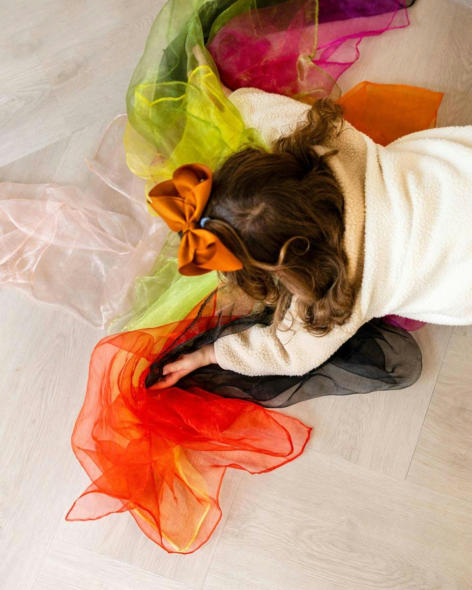 Child playing with colorful sheer fabric scarves on the floor