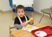 Child at a table holding a yellow object