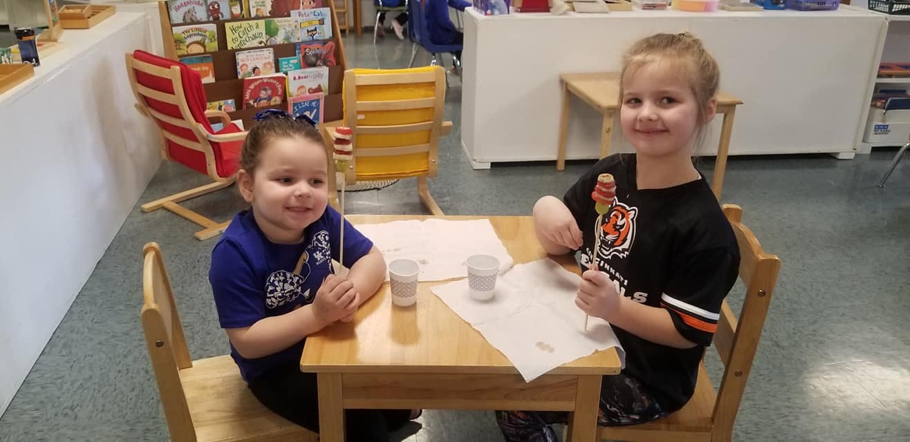 Two children sitting at a table with papers and cups