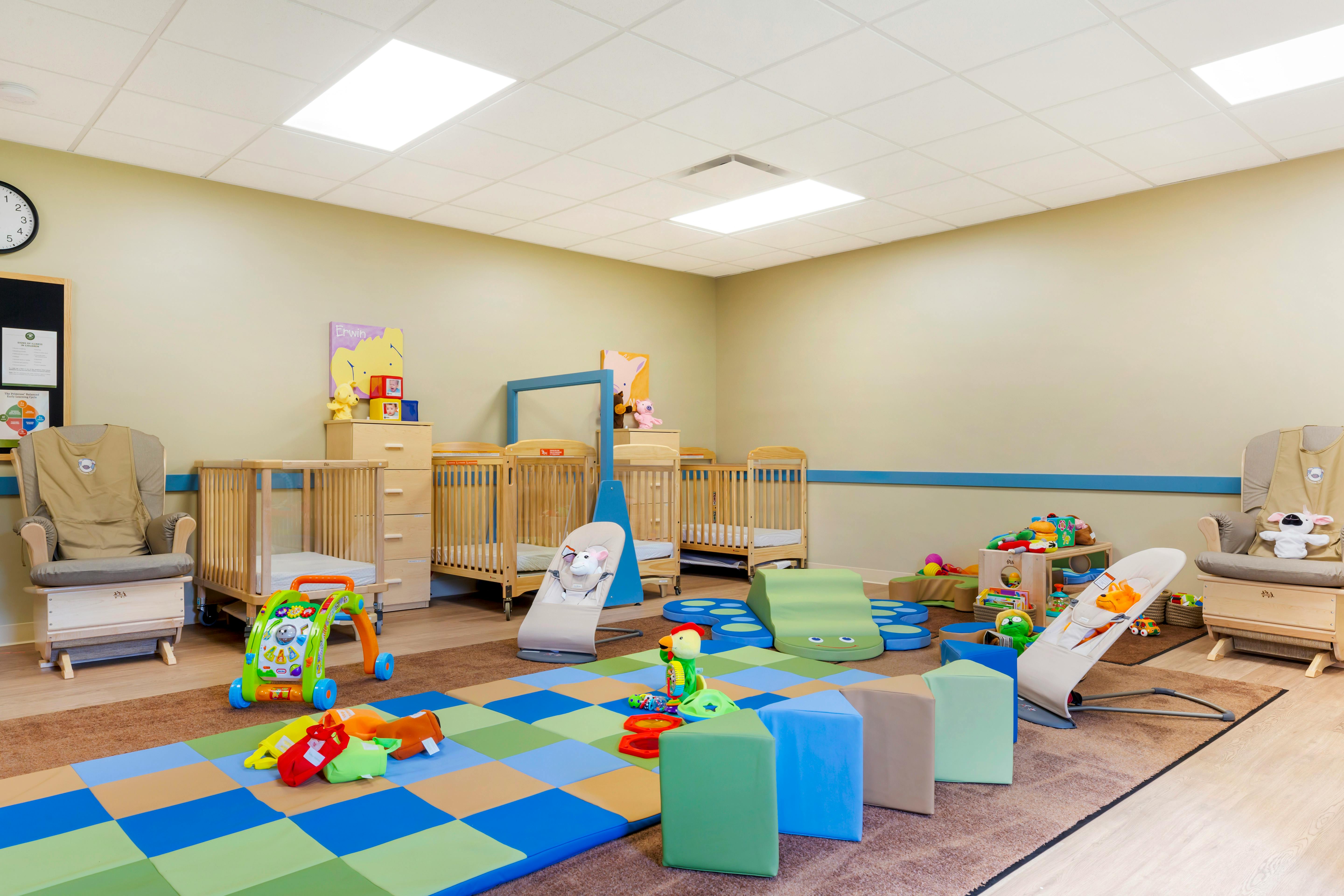 A colorful childcare room with cribs, playmats, and toys