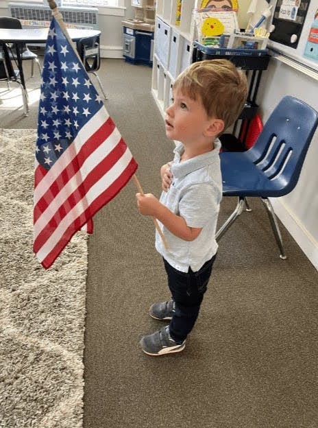 Child holding an American flag with hand over heart in a classroom