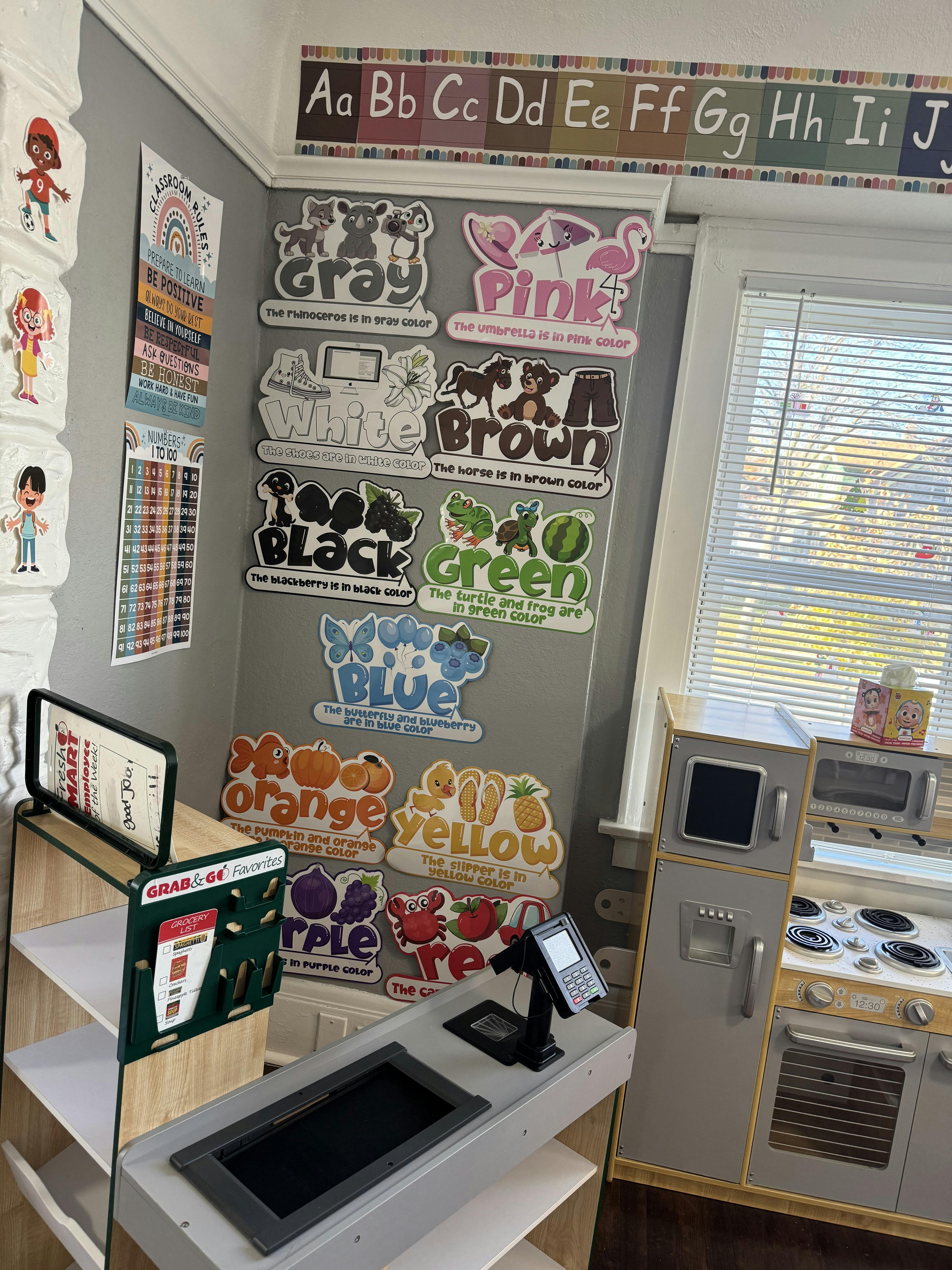 Classroom wall with alphabet and color word posters, play kitchen and store