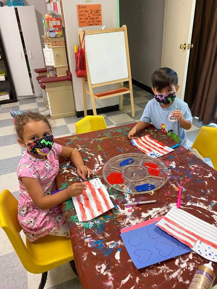 Two children wearing masks painting at a table in a classroom