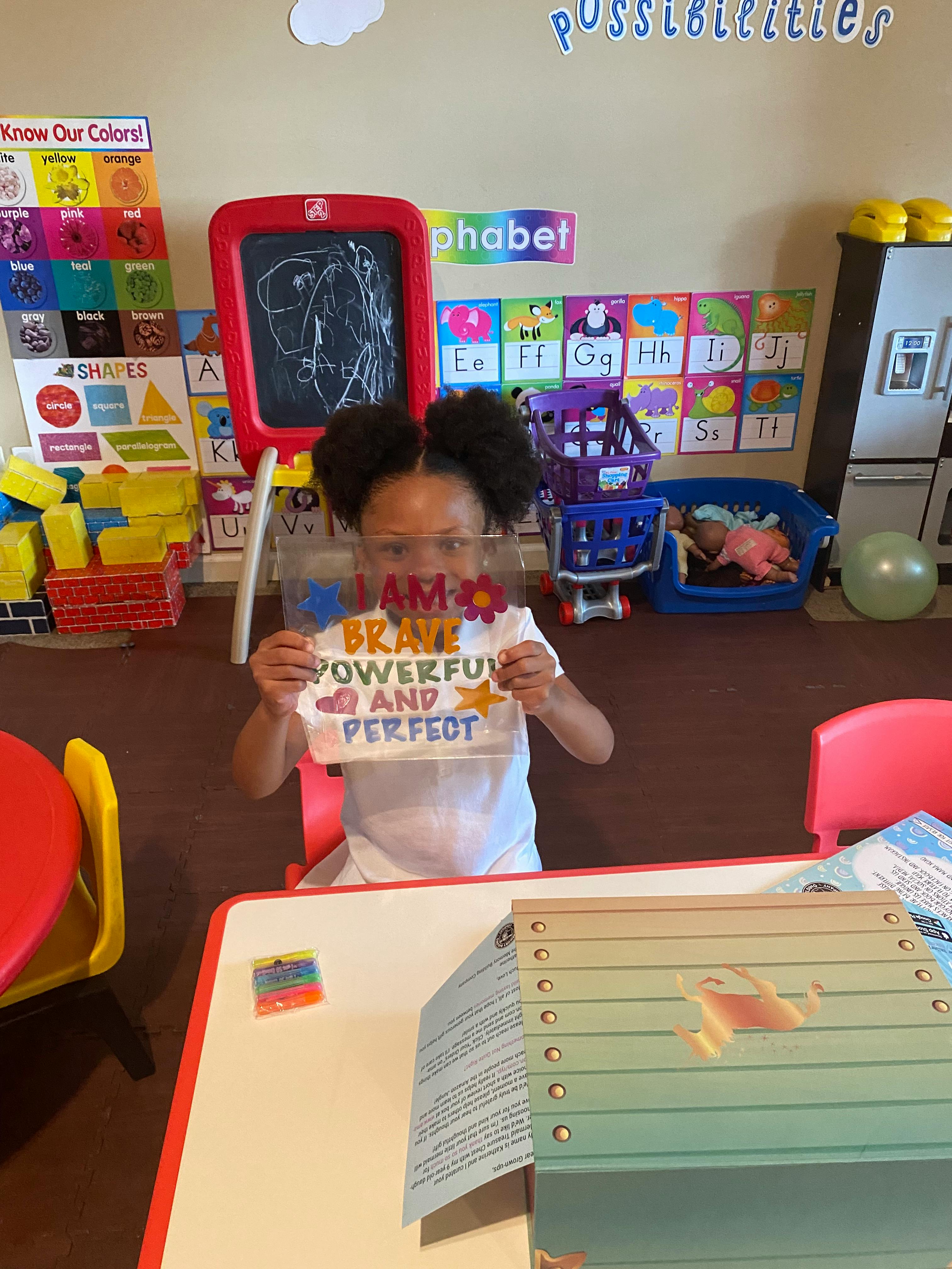 Child holding up a sign that says "I am brave, powerful, and perfect"