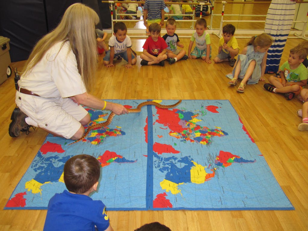 Person showing a snake to children on a world map mat