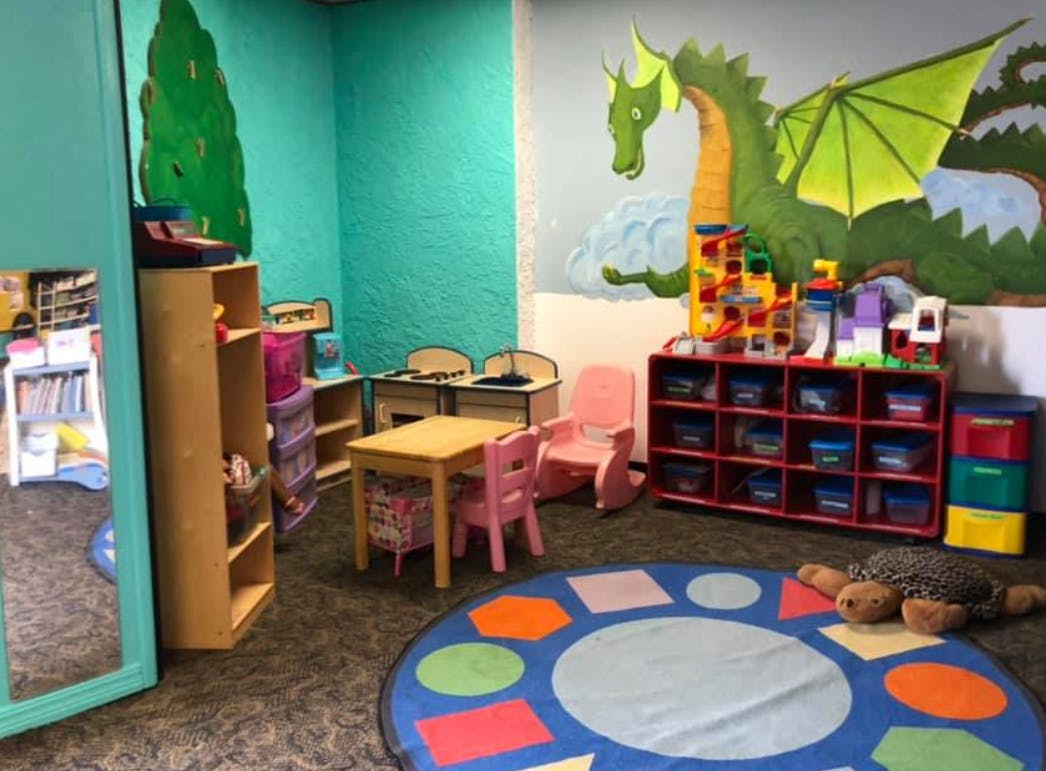 Children's play area with small tables, chairs, and a dragon mural
