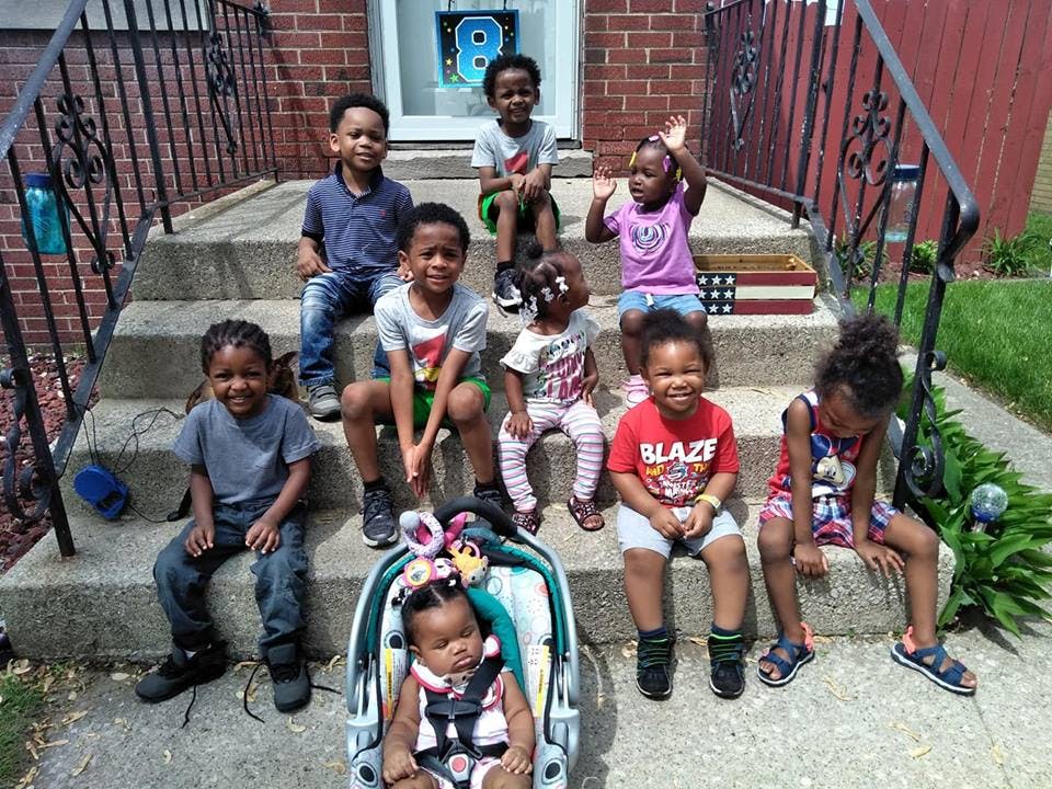 Group of children and a baby in a carrier sitting on outdoor steps
