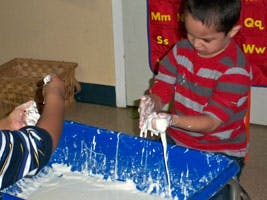 Two children playing with a white, gooey substance in a blue bin