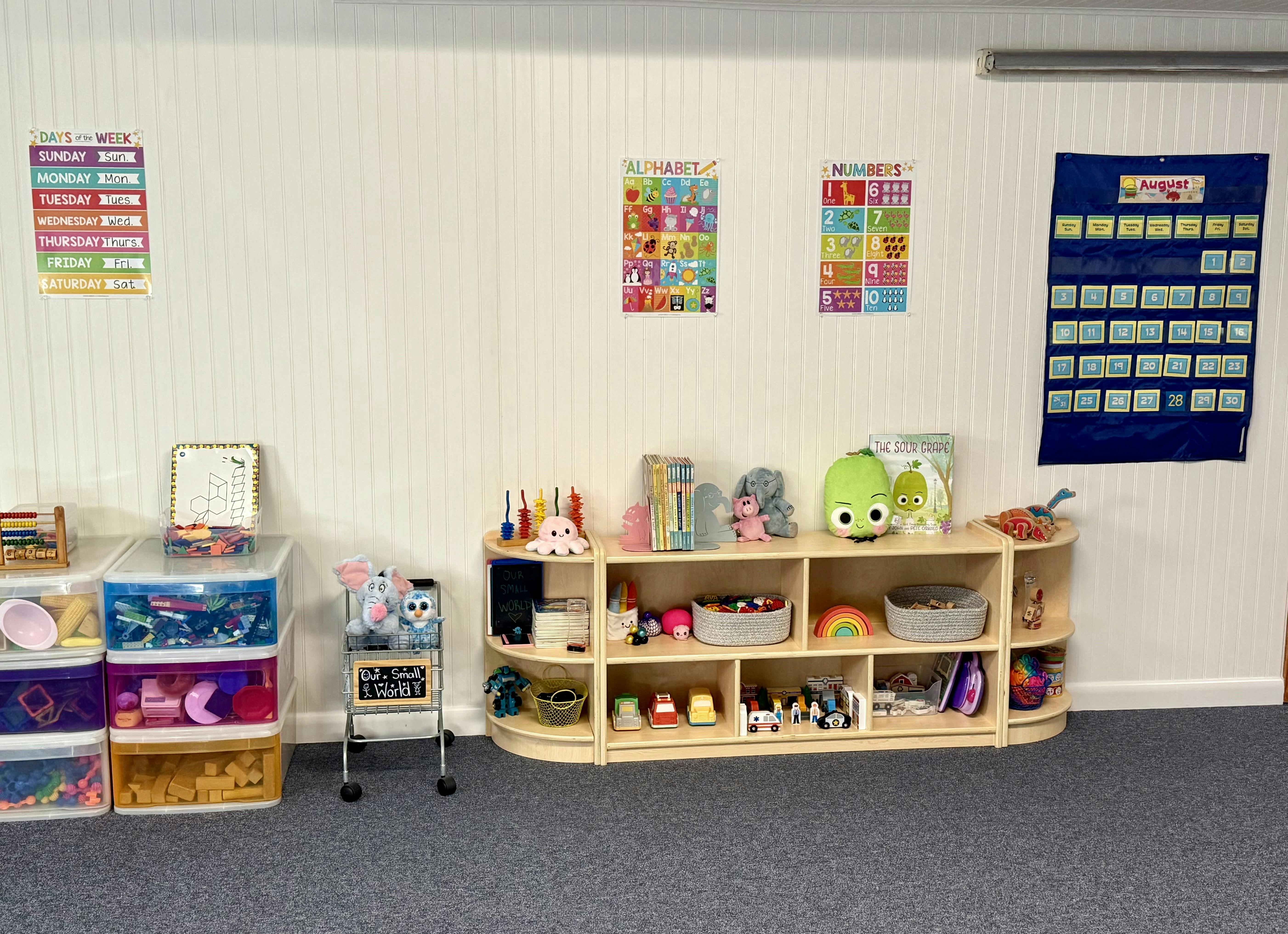 Classroom wall with calendar, alphabet and number charts, shelves with toys