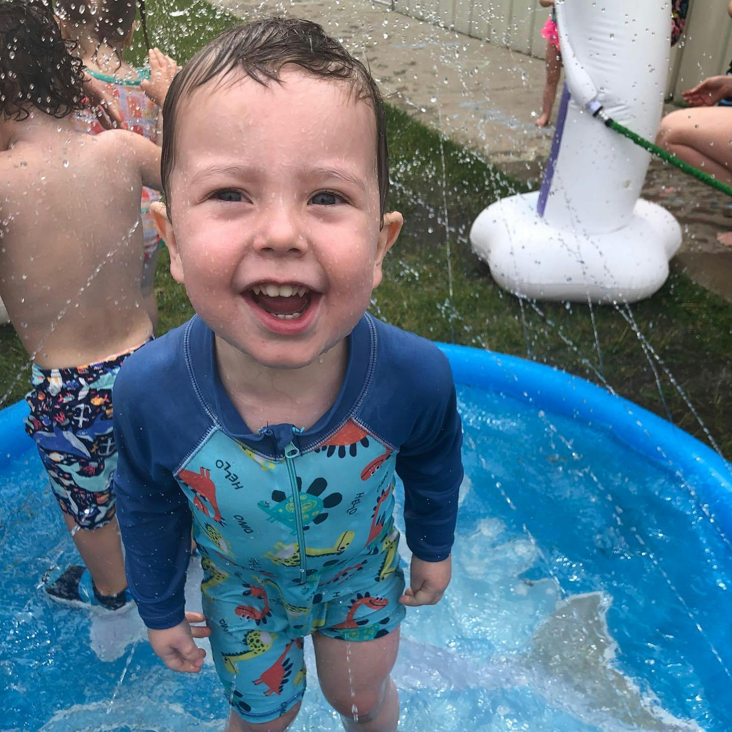 Child in a blue swimsuit standing in a wading pool with water splashing