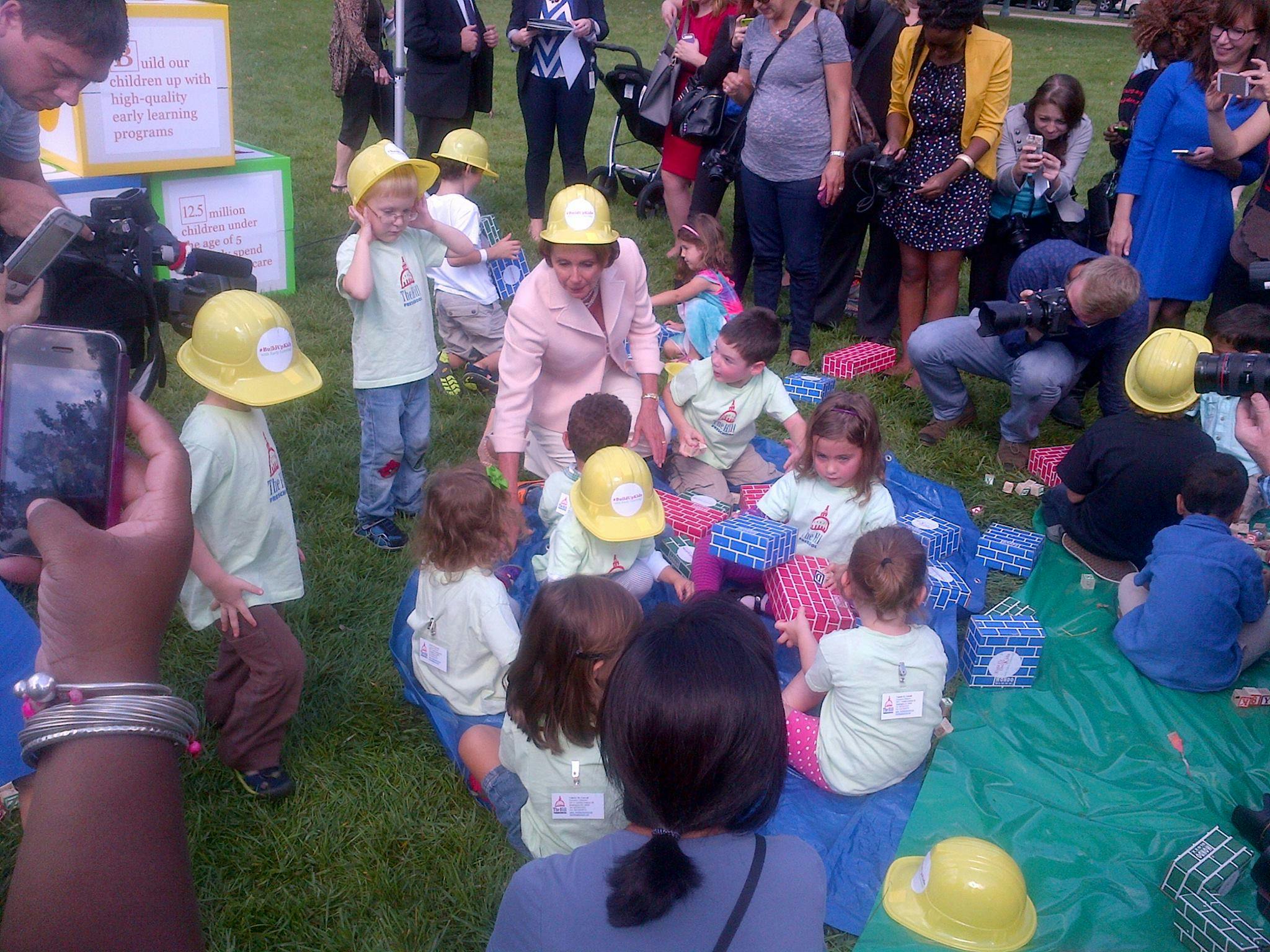 Person in pink suit with children in yellow hard hats on a green blanket