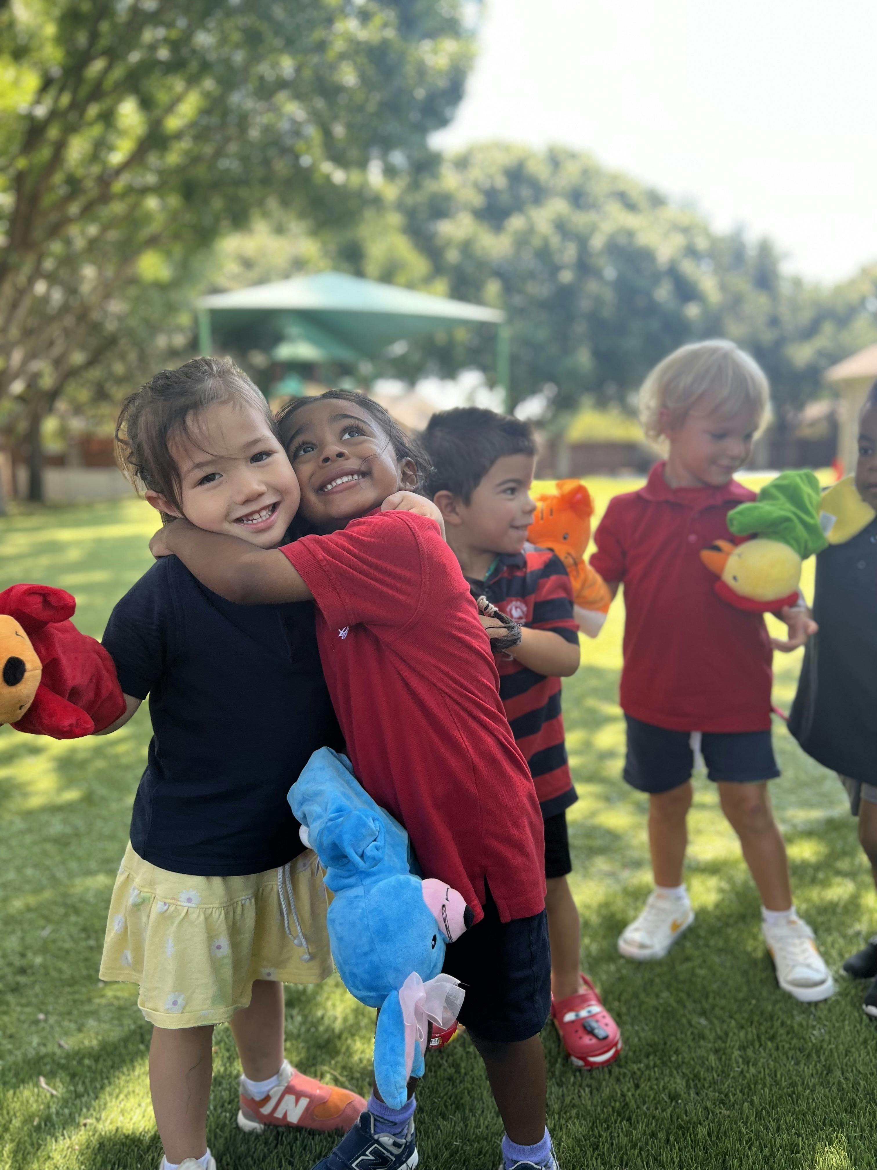 Children hugging while holding stuffed puppets on a grassy field
