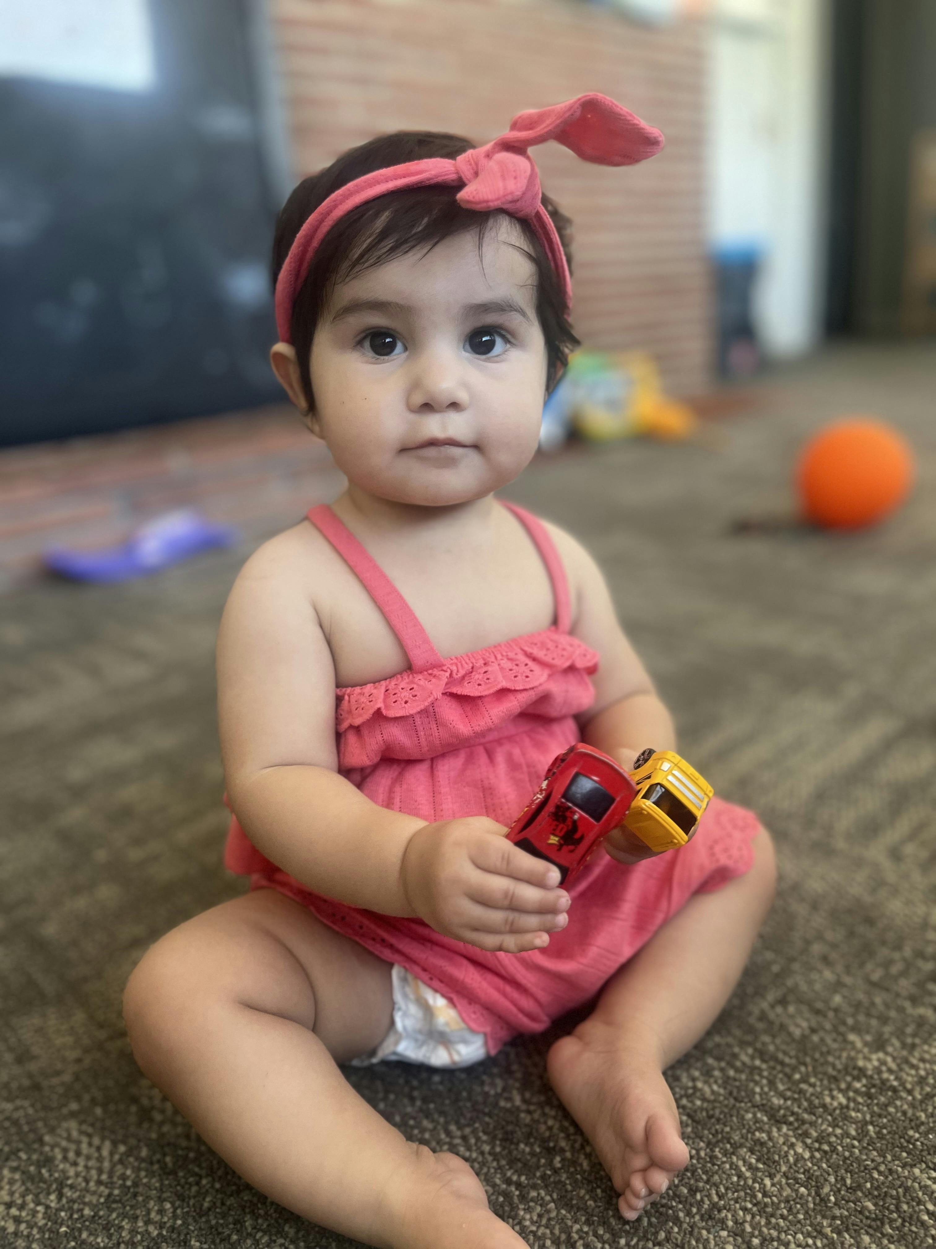 Child in pink dress holding two toy cars