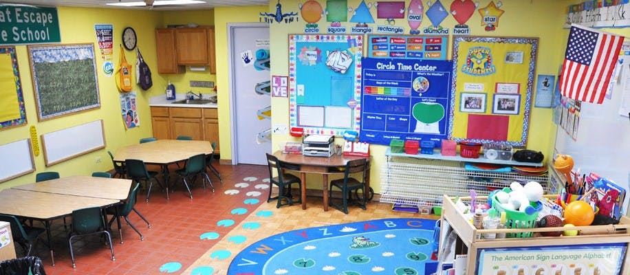 Classroom with small tables and chairs, colorful rug, and educational posters