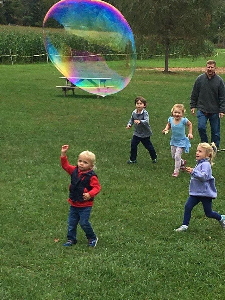 Children and an adult playing with a large bubble outdoors