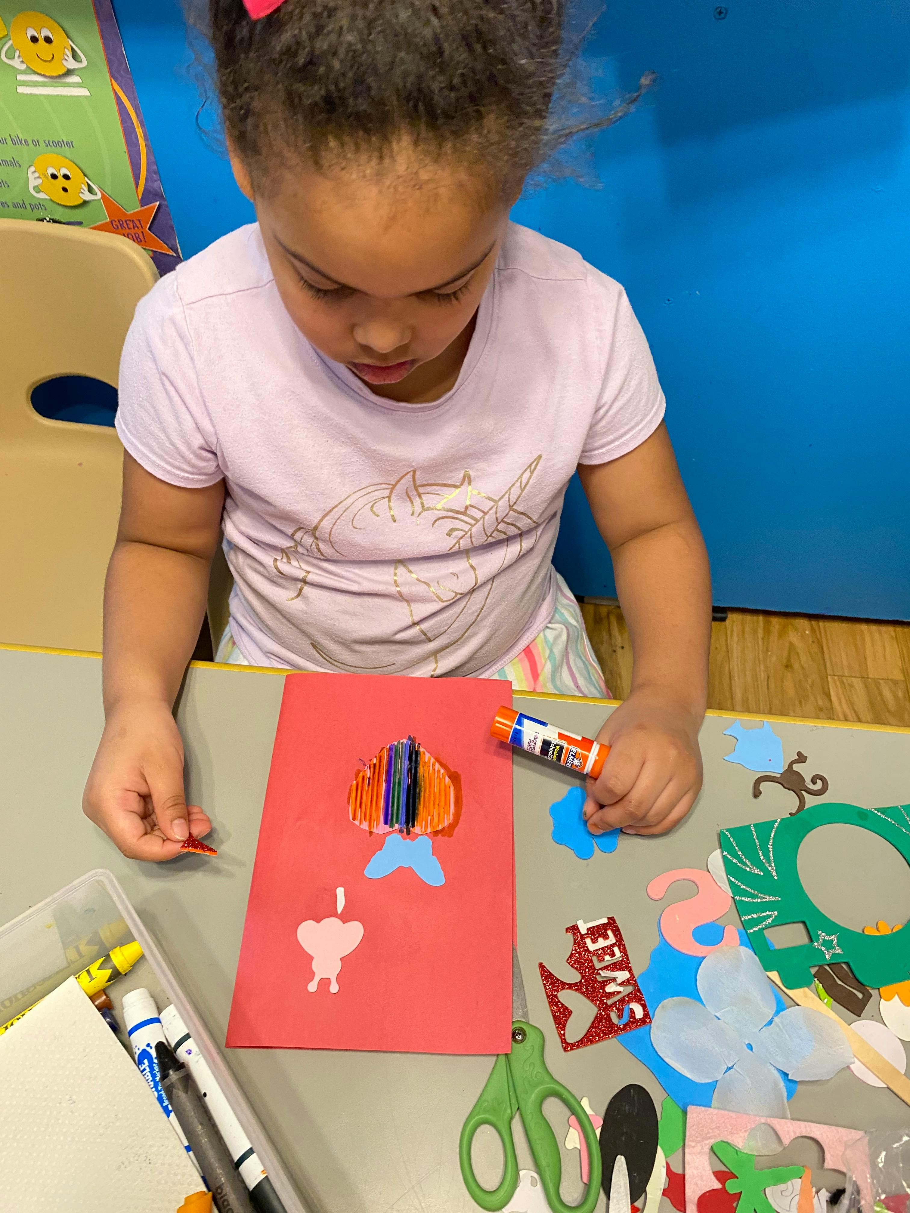 Child making a craft with paper cutouts and glue