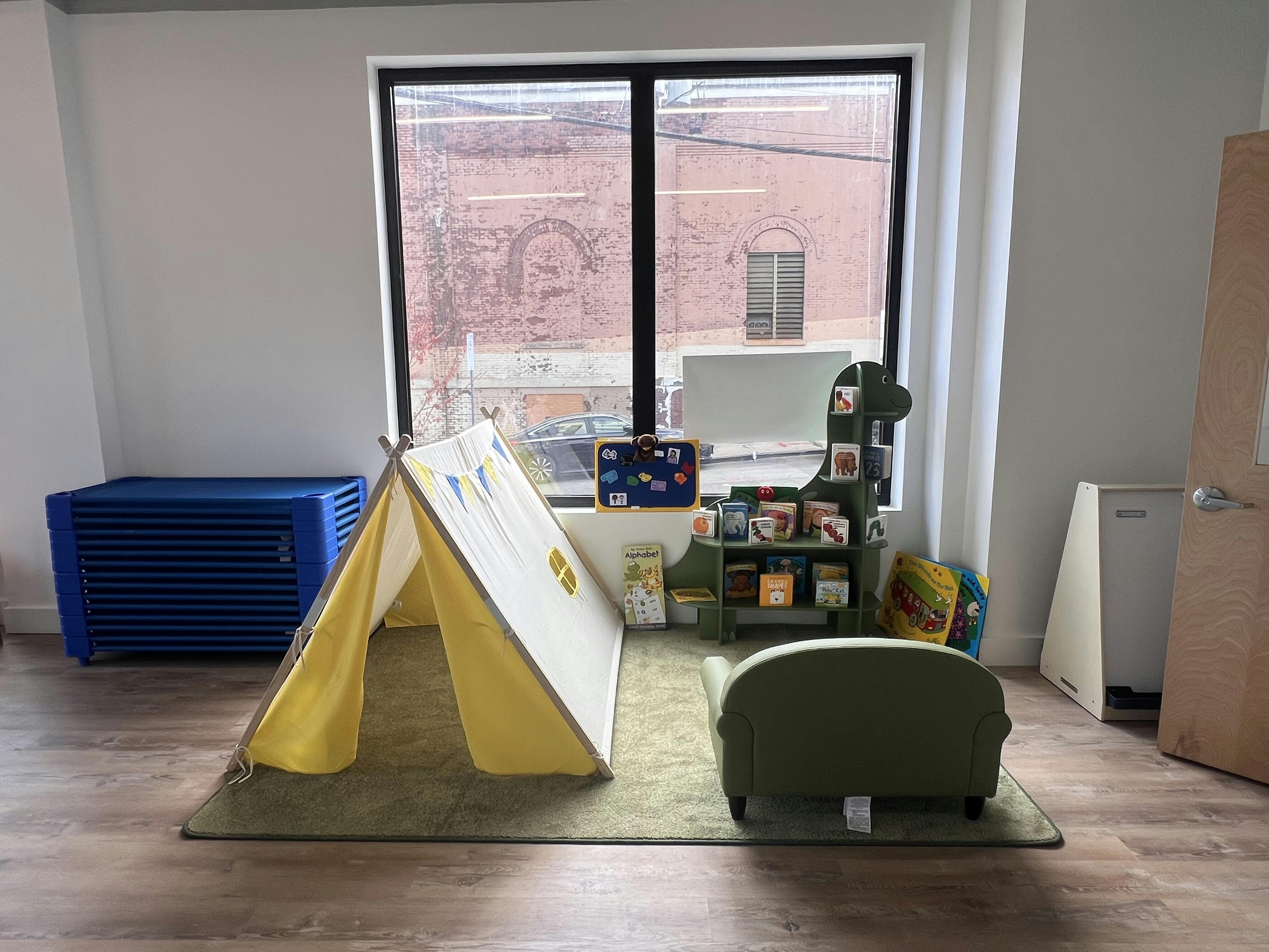 Children's reading nook with a tent, green couch, and dinosaur-shaped bookshelf