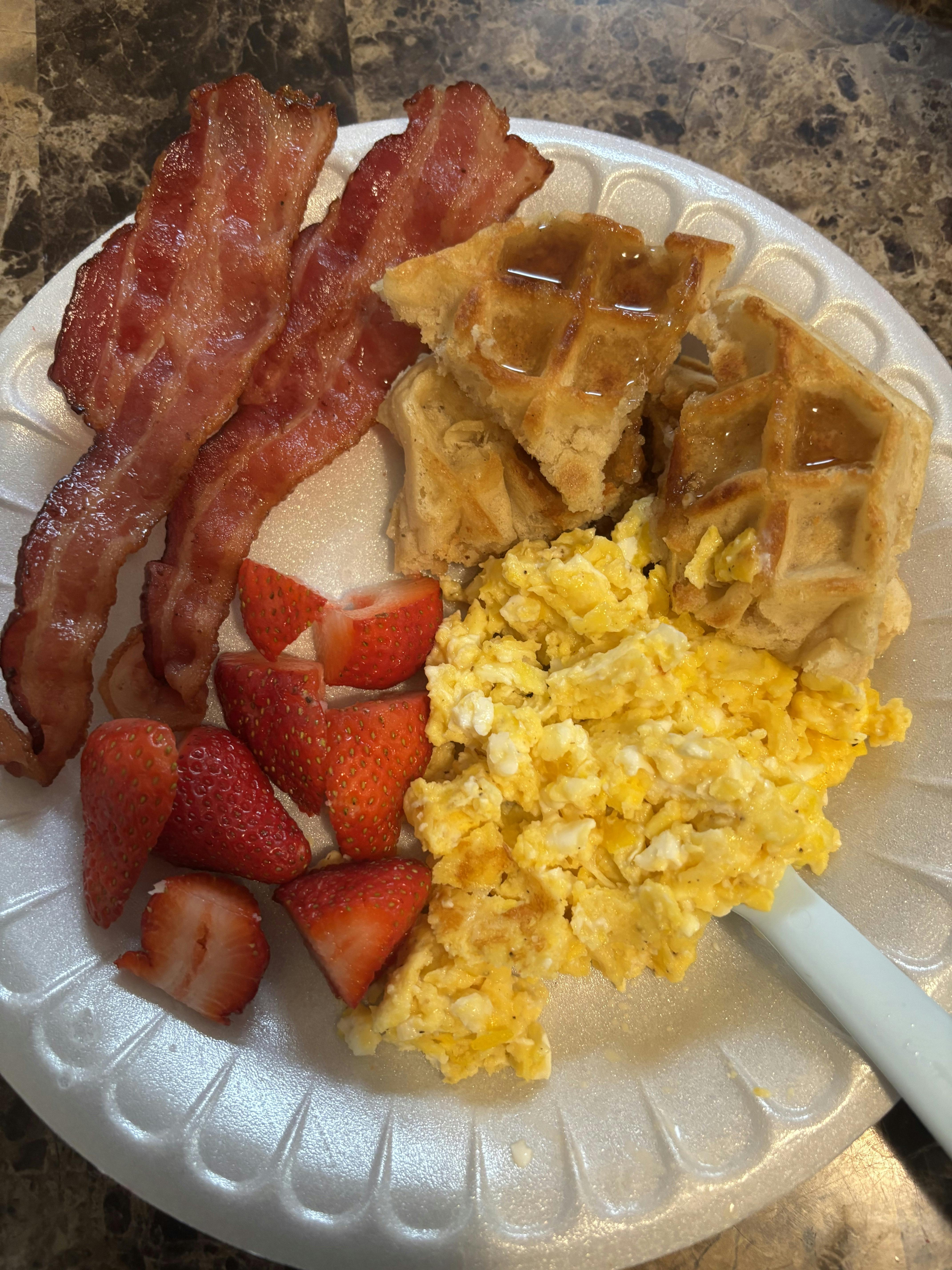 Breakfast plate with bacon, waffles, scrambled eggs, and strawberries