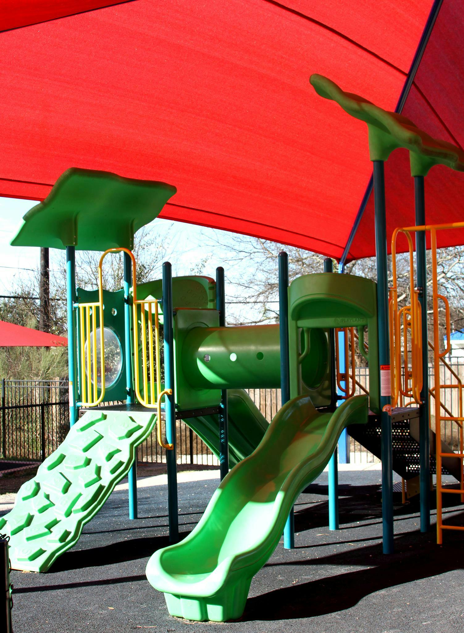 Green playground equipment with slides under a red shade canopy