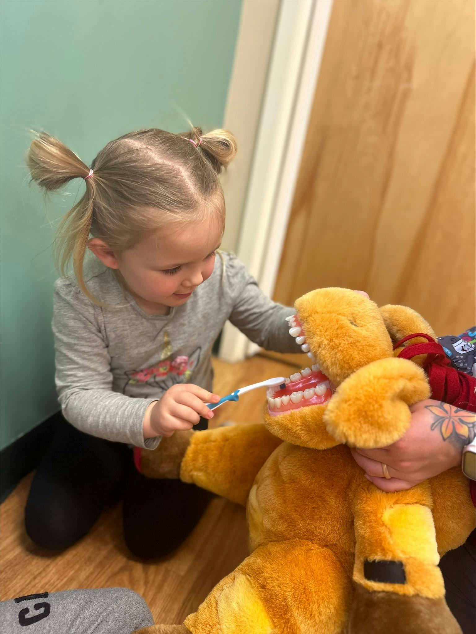 Child brushing teeth of a large stuffed animal with exposed teeth model