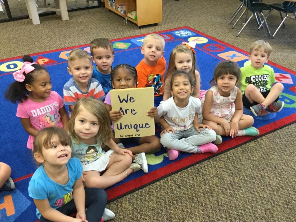 Group of children sitting on a rug, one holding a sign that says "We Are Unique"