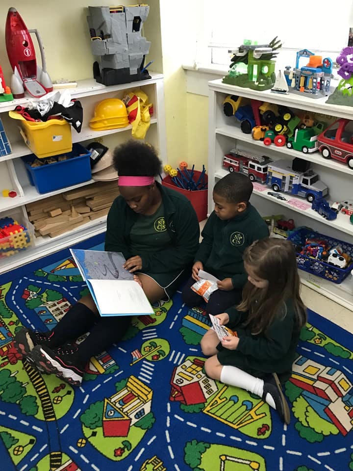 Three children sitting on a rug, one reading a book
