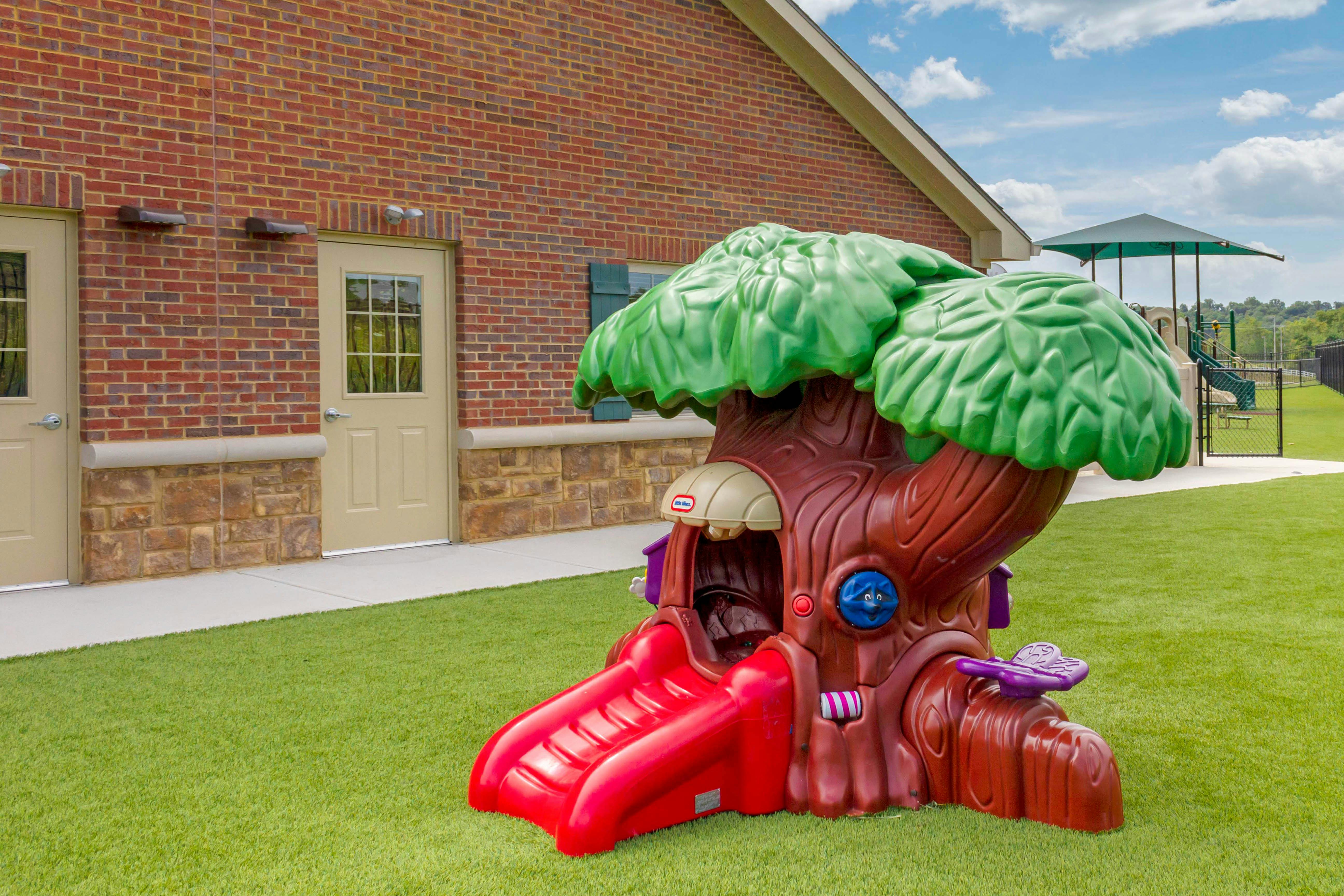 Plastic treehouse playground with a red slide on a grassy lawn