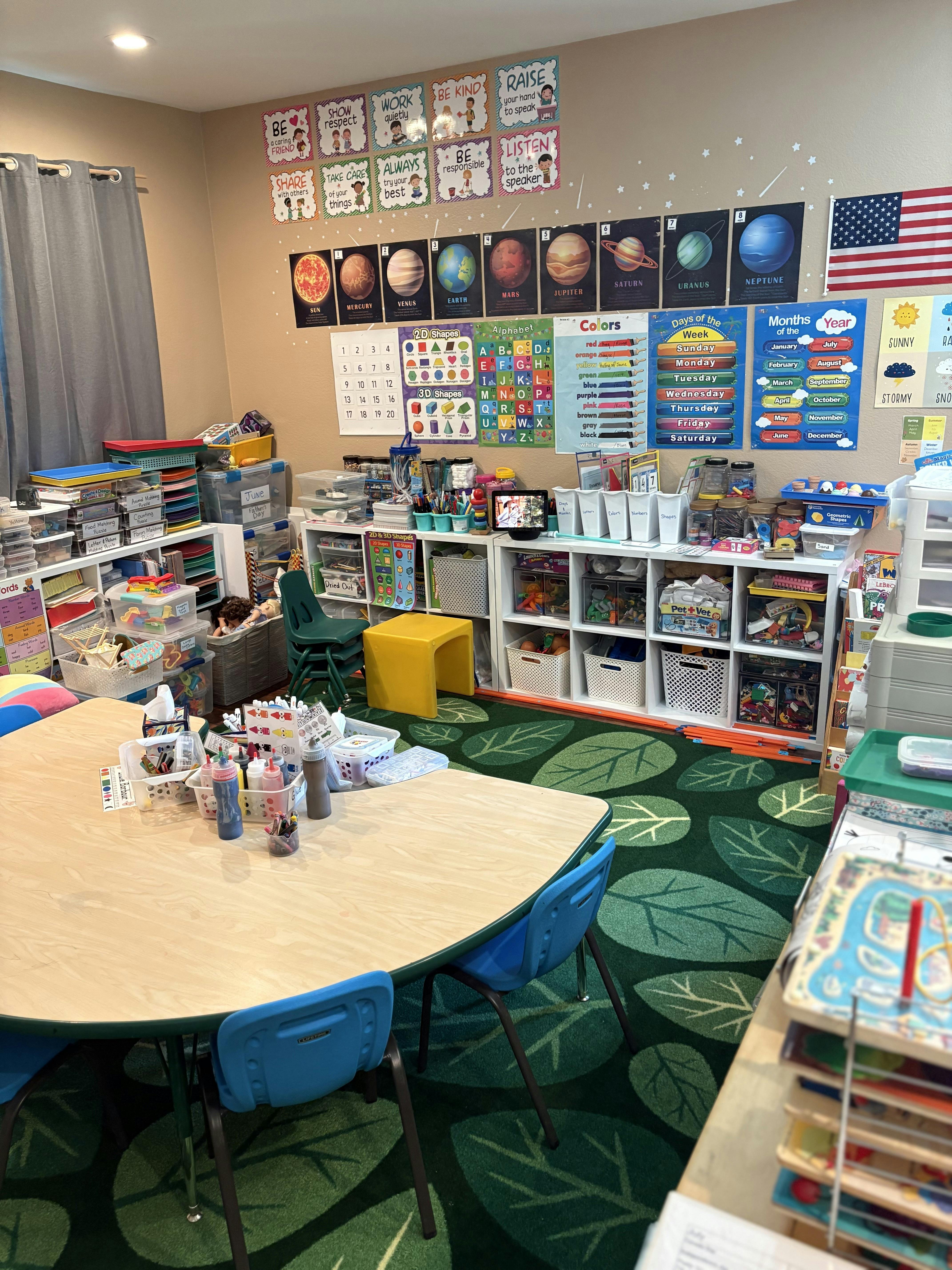 Classroom with tables, chairs, shelves, and educational posters on the wall