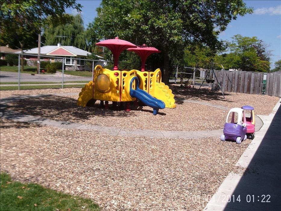 Playground with yellow and blue slide and two toy cars on wood chips