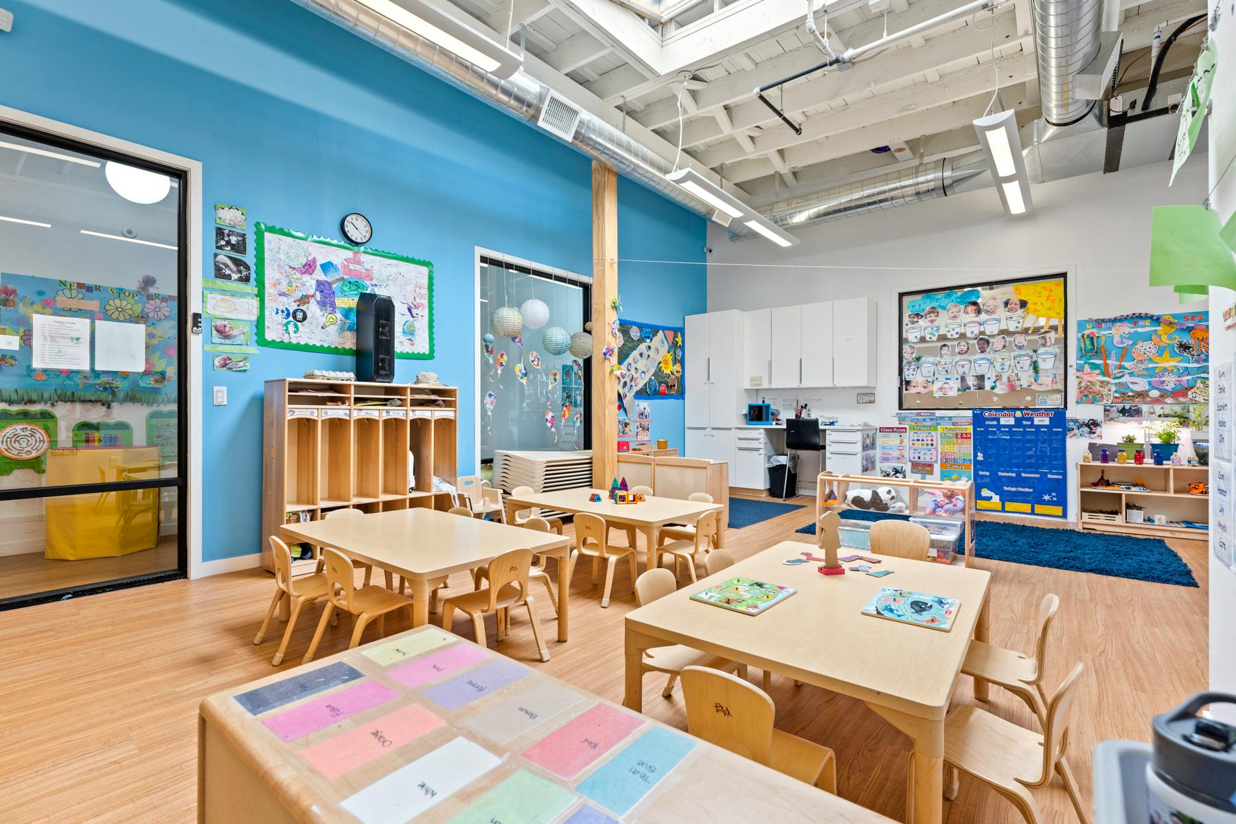 Classroom with small tables and chairs, blue walls, and a large window
