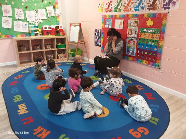 Adult sitting on a chair, reading to a group of children seated on a rug