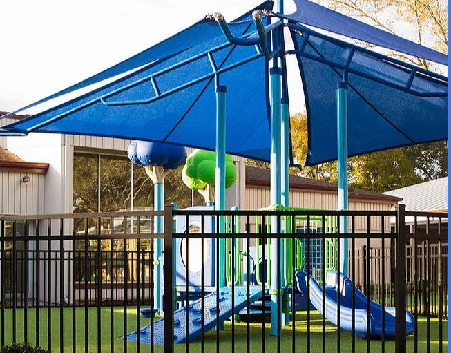 Playground with blue shade structure and slides behind a black fence