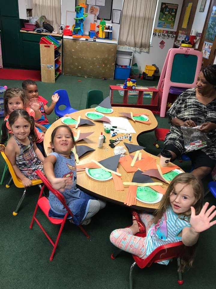 Children and an adult at a table with craft supplies in a classroom