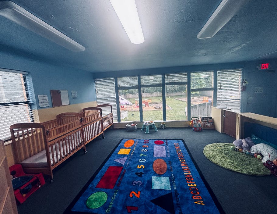 Cribs and colorful educational rug in a daycare classroom
