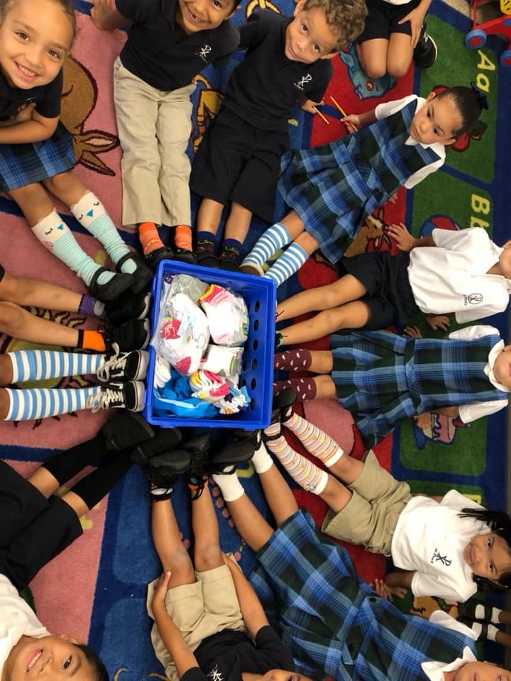 Children lying in a circle with their feet pointing towards a blue bin of socks