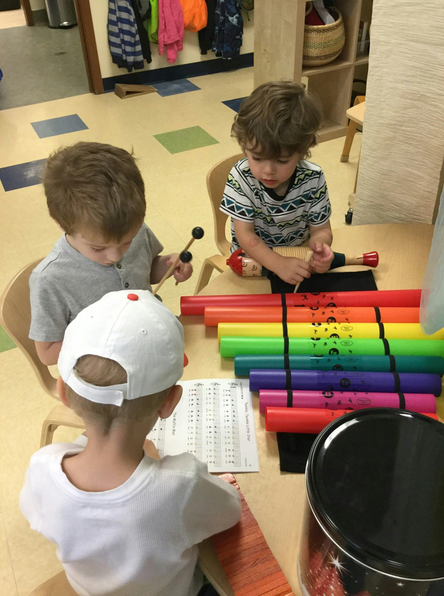 Three children playing with musical instruments at a table in a classroom