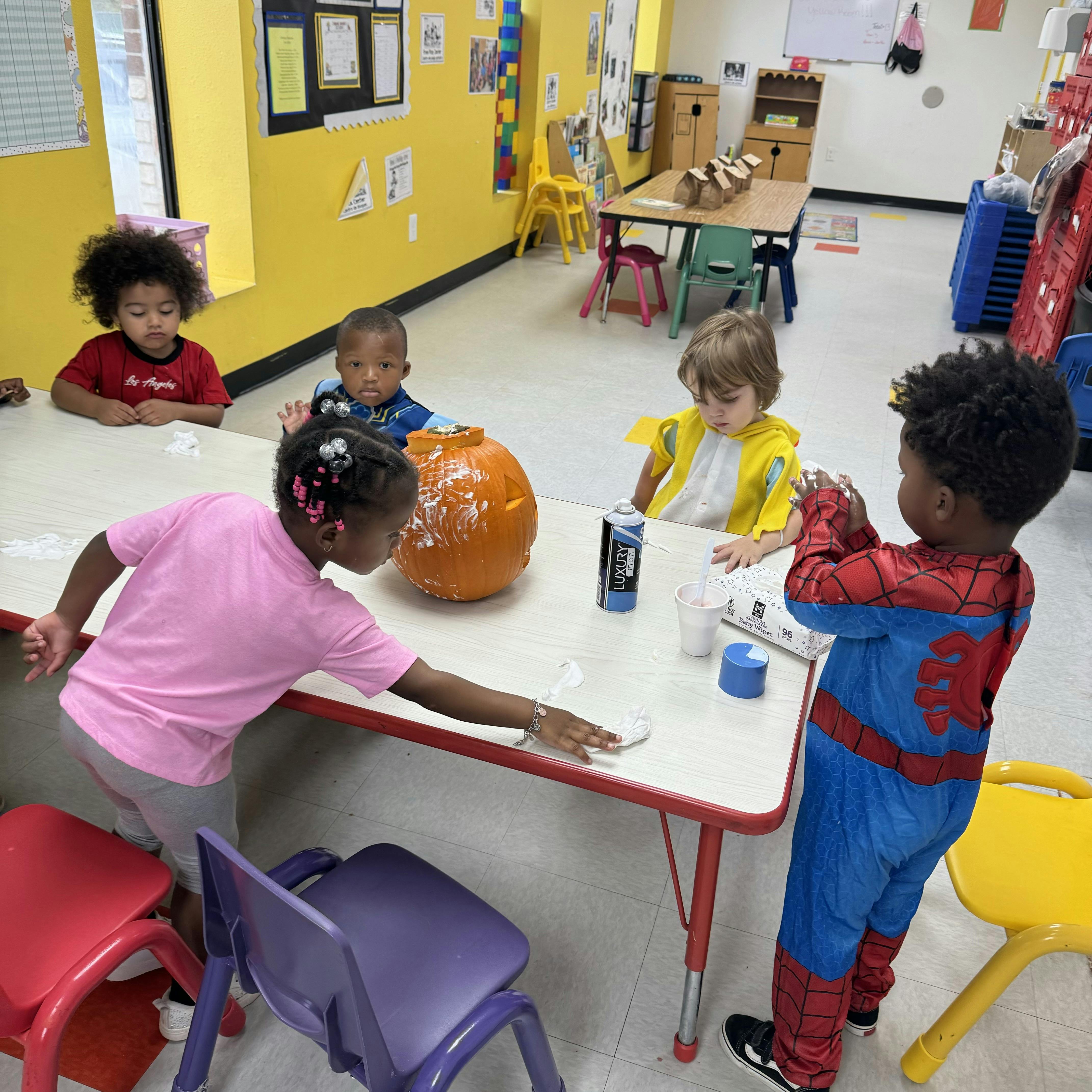 Children gathered around a table with a pumpkin in a classroom