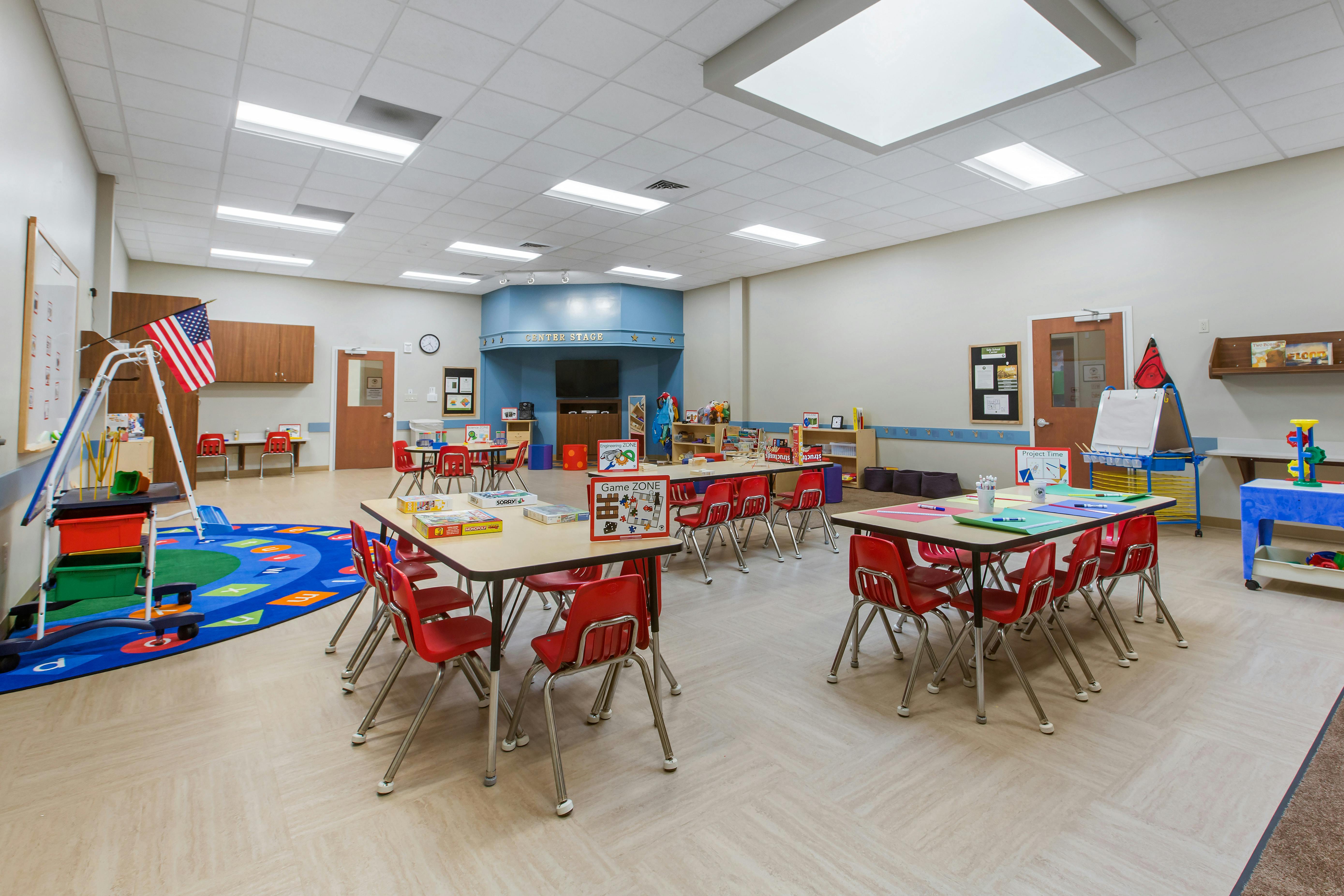 Classroom with multiple tables and red chairs, and a play area