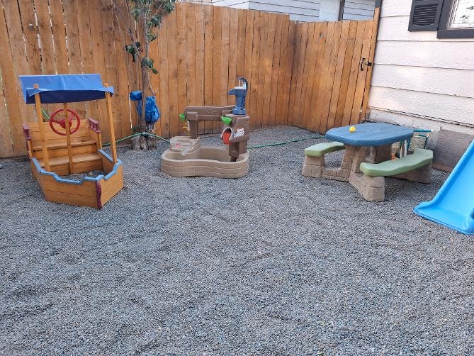 Childrens play area with plastic equipment on a gravel backyard