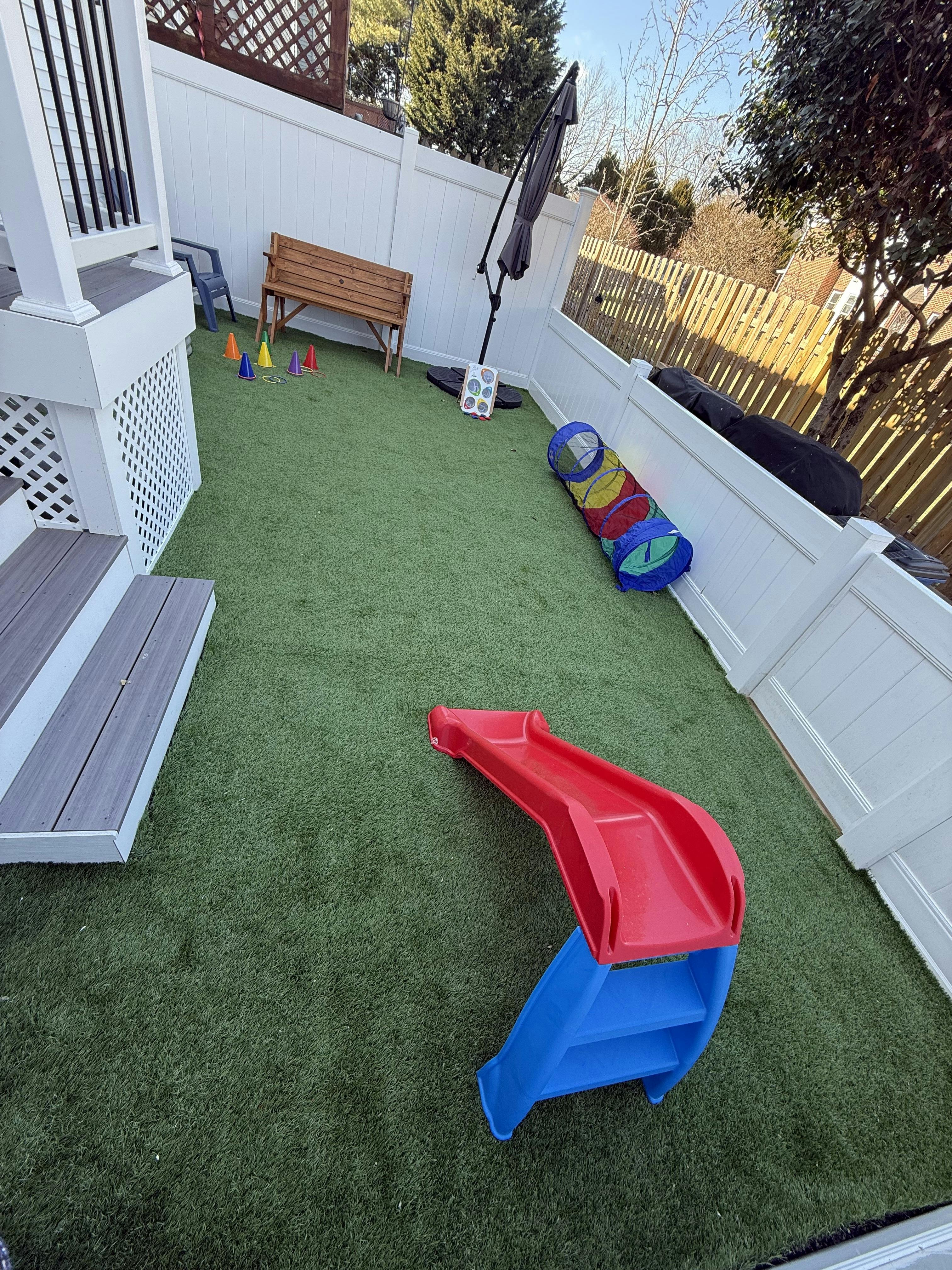 Red and blue slide on artificial grass with a play tunnel and cones