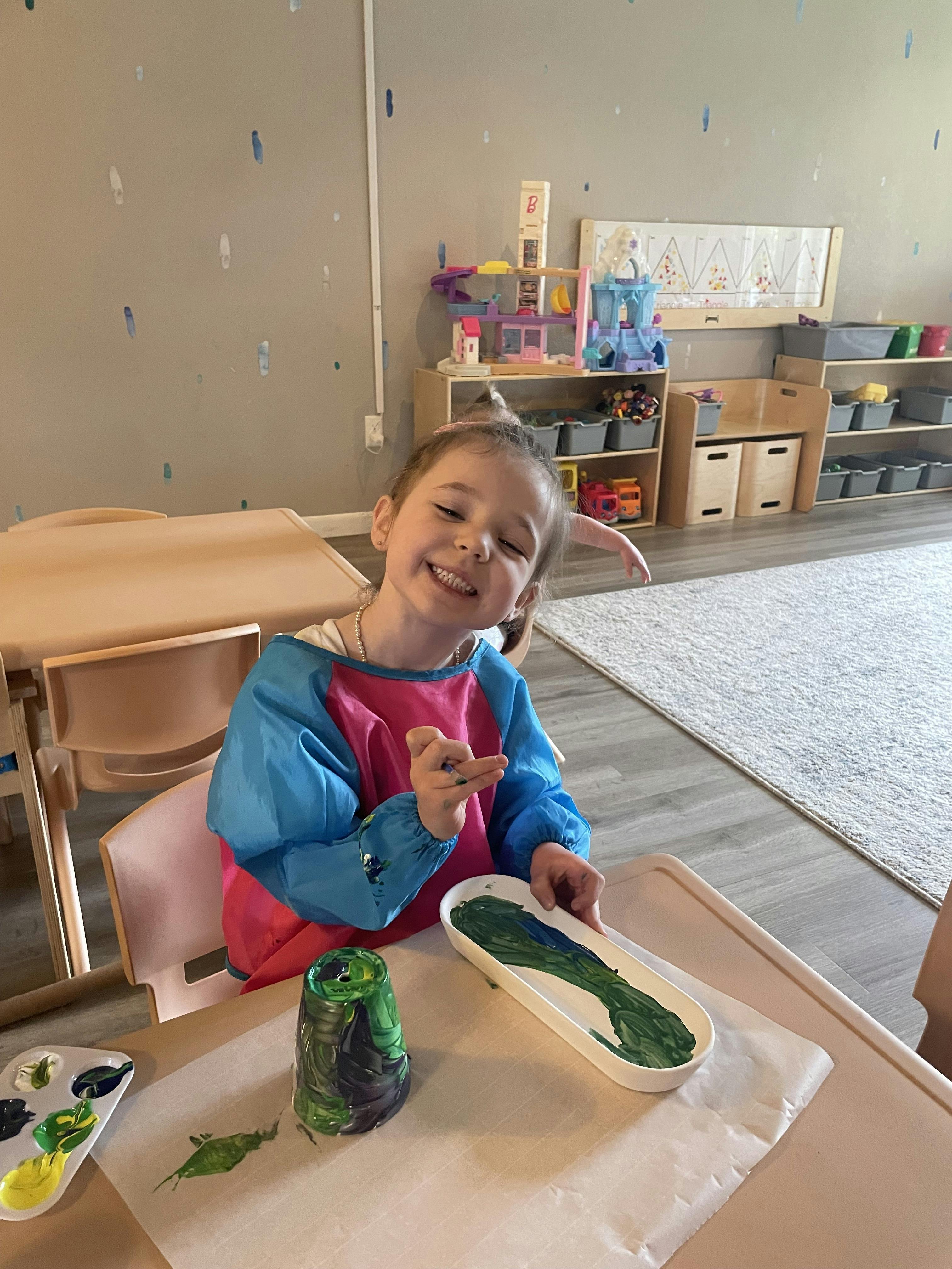 Child in a smock at a table with paint and painted crafts