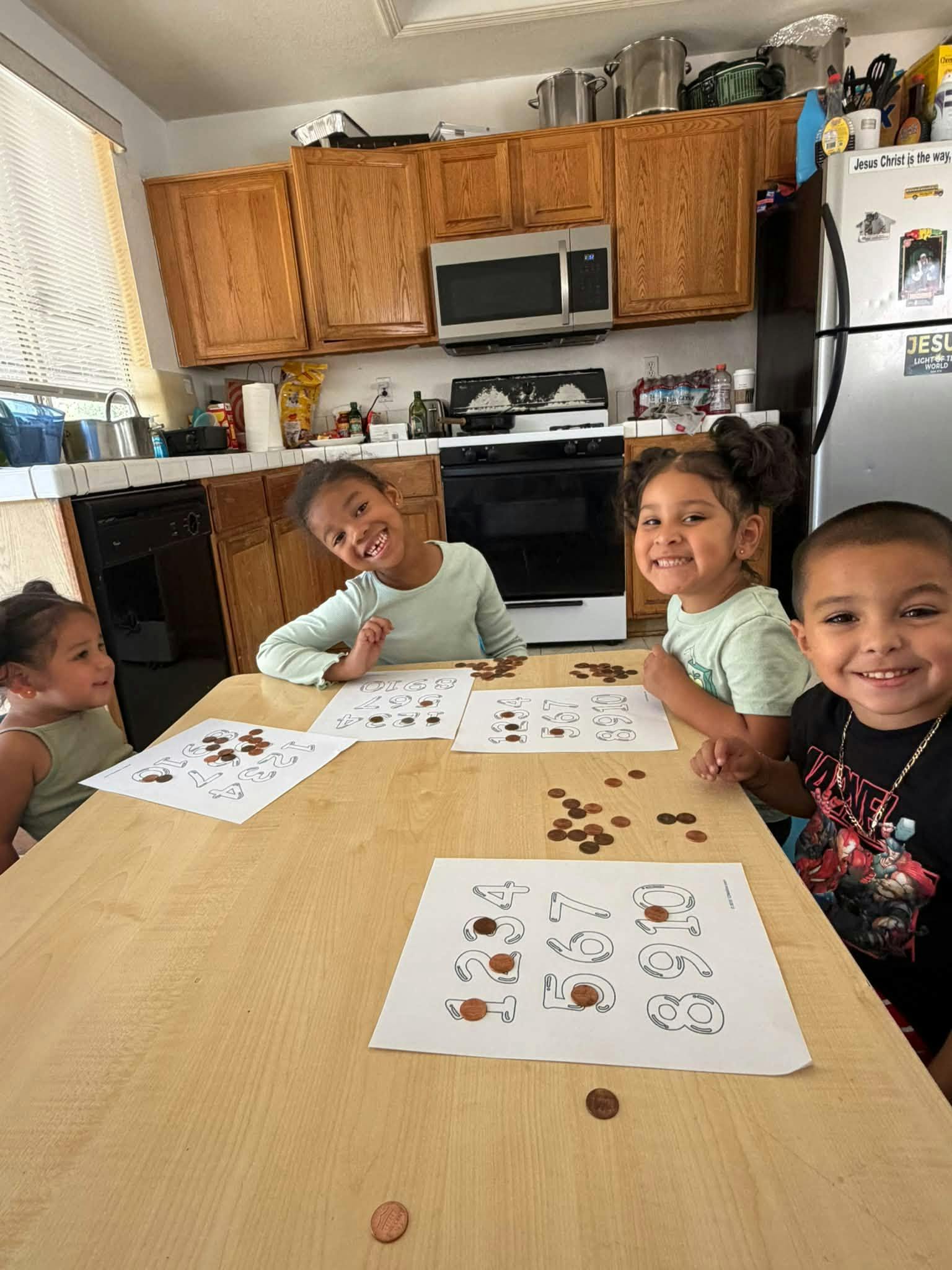Four children sitting at a kitchen table placing pennies on numbered worksheets