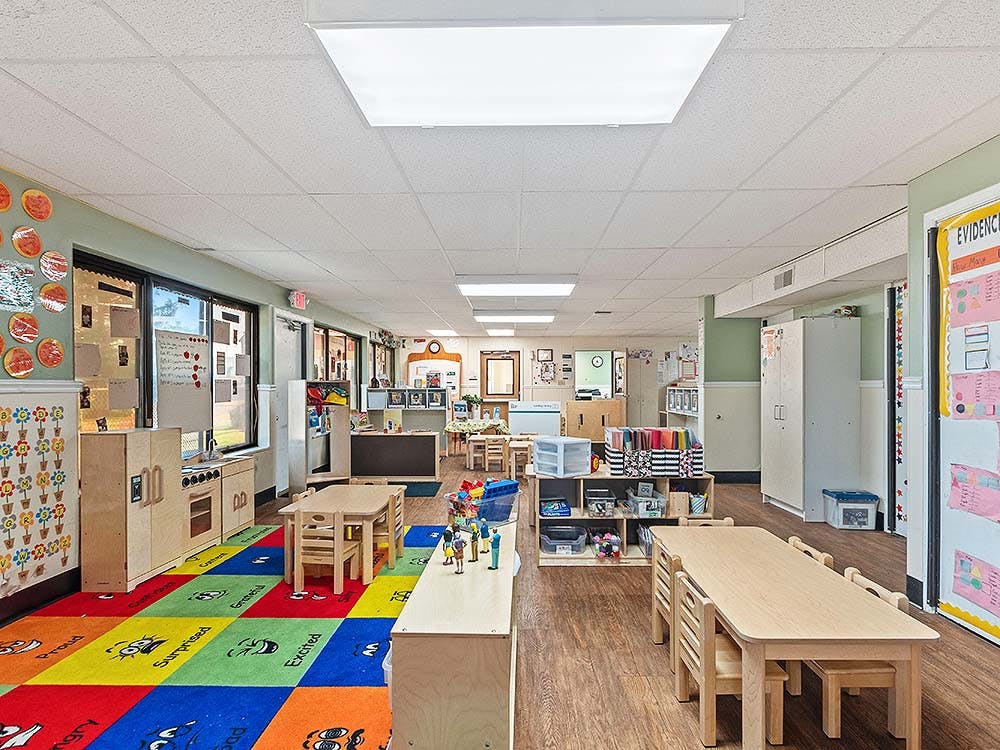 Classroom with play kitchen, colorful rug with faces, and small tables