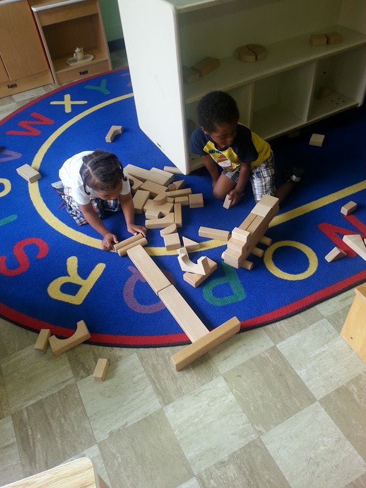 Two children playing with wooden blocks on a rug