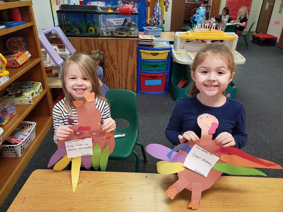 Two children holding up paper turkey crafts in a classroom
