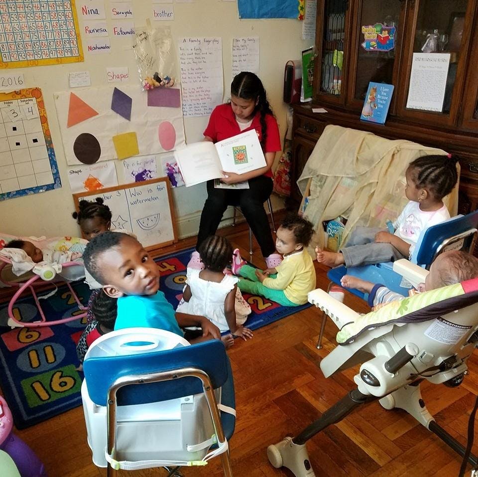 Person reading a book to a group of children in a room