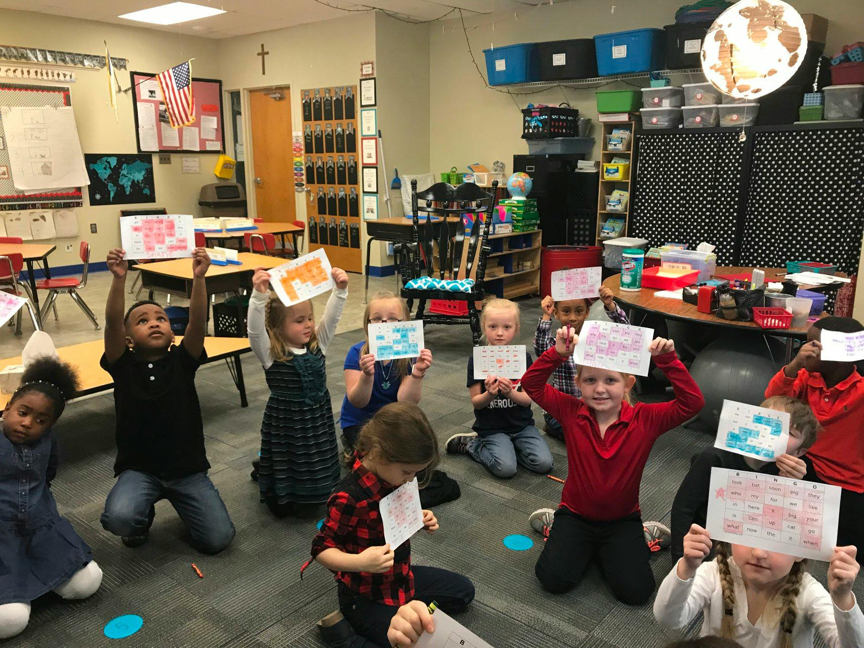 Children sitting on the floor holding up drawings in a classroom